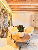Un interior moderno con pared de ladrillo, dos sillas blancas, una mesa redonda de madera y una planta en maceta.