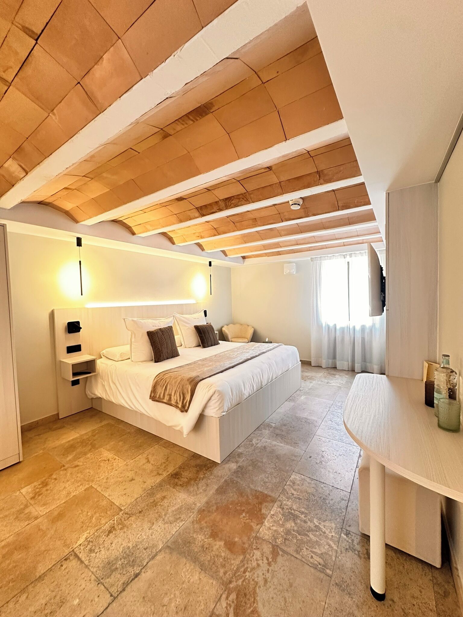 Un dormitorio con una cama grande, una mesita de noche, un escritorio y un techo con vigas de madera.