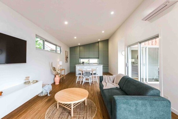 Uma sala de estar moderna com um sofá, uma mesa de jantar e uma cozinha ao fundo.
