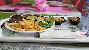 Un plateau contenant une assiette de nourriture comprenant des frites, une salade et un plat de viande, accompagné d’une bouteille d’eau.