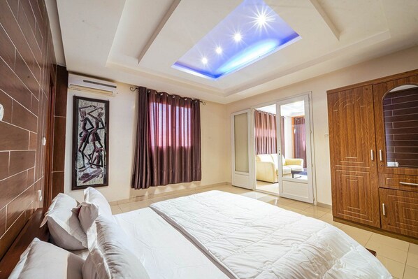 A hotel room with a large bed, a ceiling skylight, a wooden wardrobe, and a door leading to a balcony. - Hotel Darou Khoudoss (Dakar)