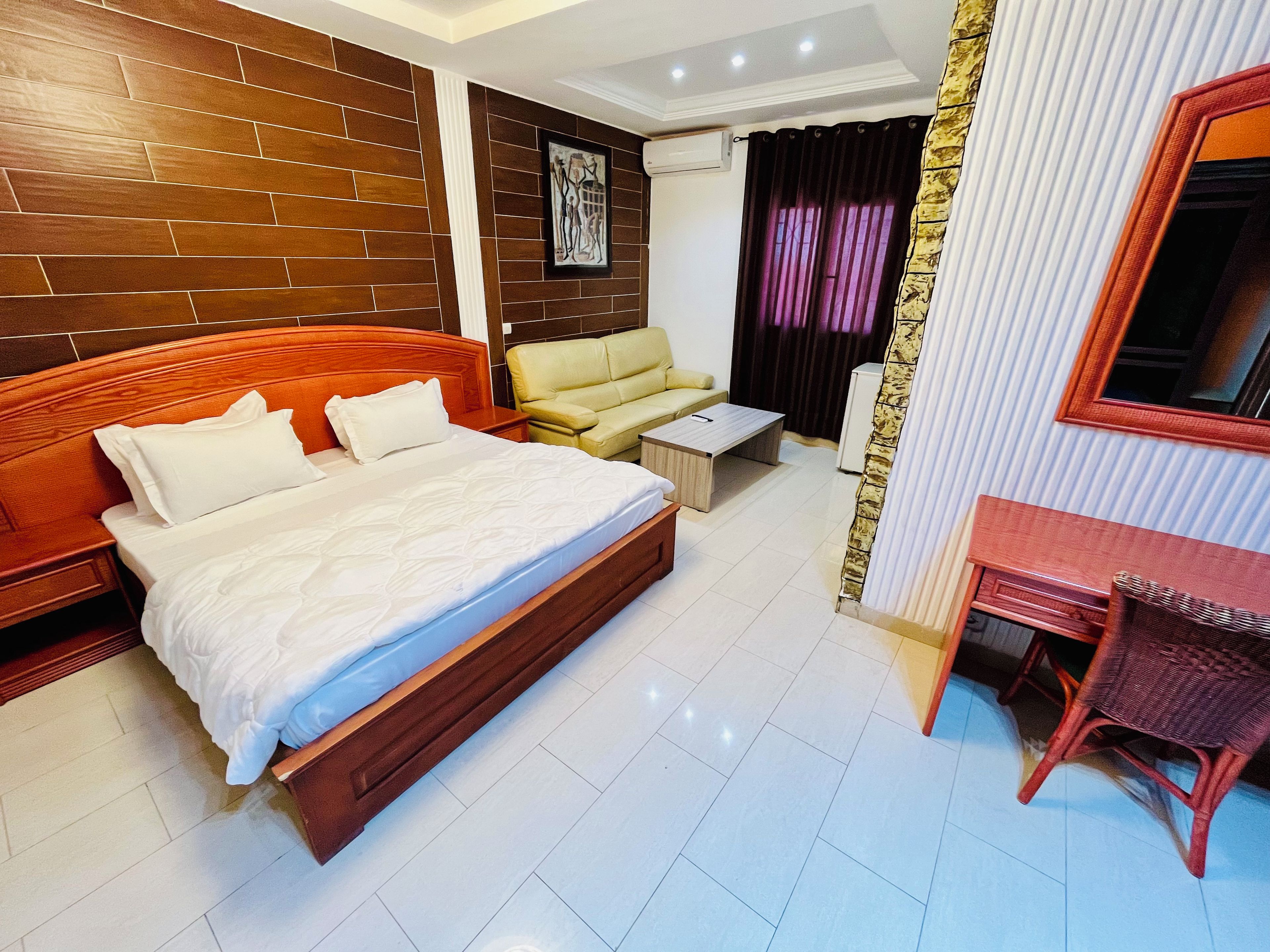 Quarto de hotel com uma cama grande, um sofá, uma mesa pequena, uma escrivaninha e um espelho.