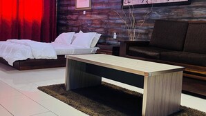 A modern living room with a wooden coffee table, a sofa, and a bed with white bedding. - Hotel Darou Khoudoss (Dakar)
