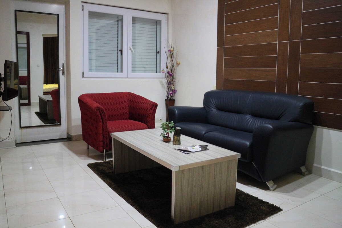 A living room with a red armchair, a black leather sofa, a wooden coffee table, and a small potted plant.