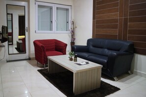 Un salon avec un fauteuil rouge, un canapé en cuir noir, une table basse en bois et une petite plante en pot.