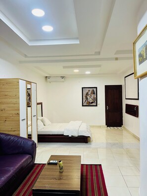 A modern room with a bed, a wooden wardrobe, a purple sofa, a coffee table, and a framed picture on the wall. - Hotel Darou Khoudoss (Dakar)