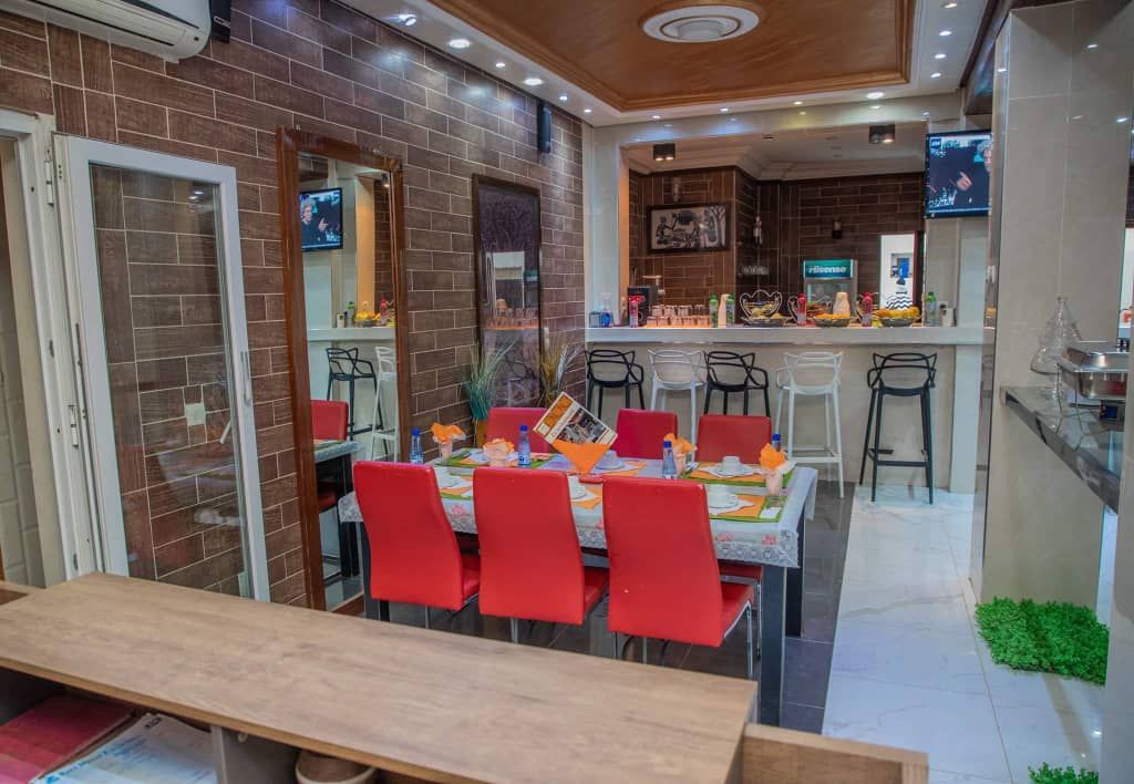 Un comedor con una mesa de madera larga y sillas rojas, una cocina con mostrador y taburetes, y un televisor fijado en la pared.