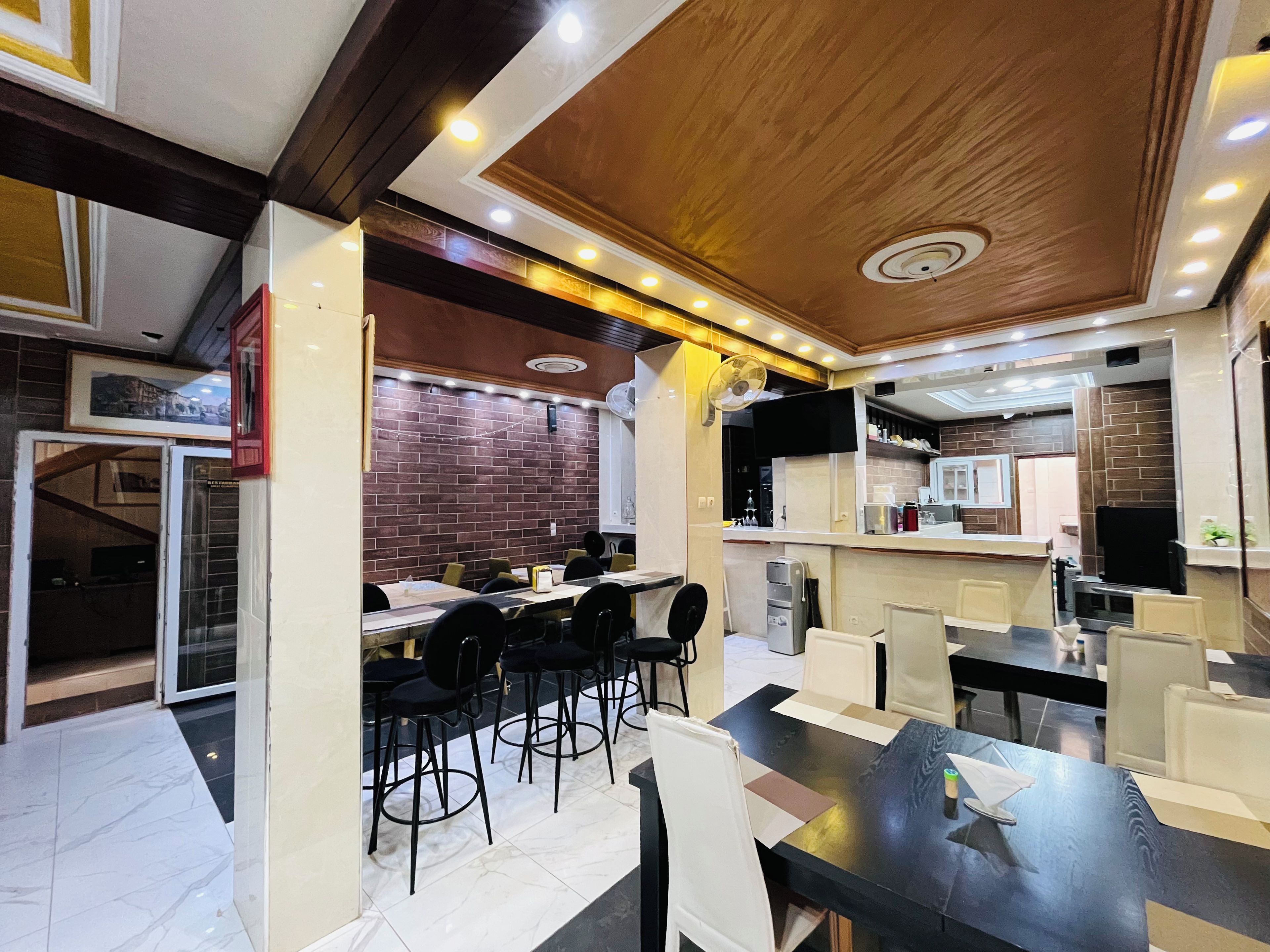 Um restaurante moderno com parede de tijolos, teto de madeira e várias mesas e cadeiras.