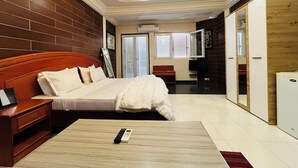 A hotel room with a wooden headboard bed, a bedside table, a flat-screen TV, a wardrobe, and a small desk with a chair. - Hotel Darou Khoudoss (Dakar)
