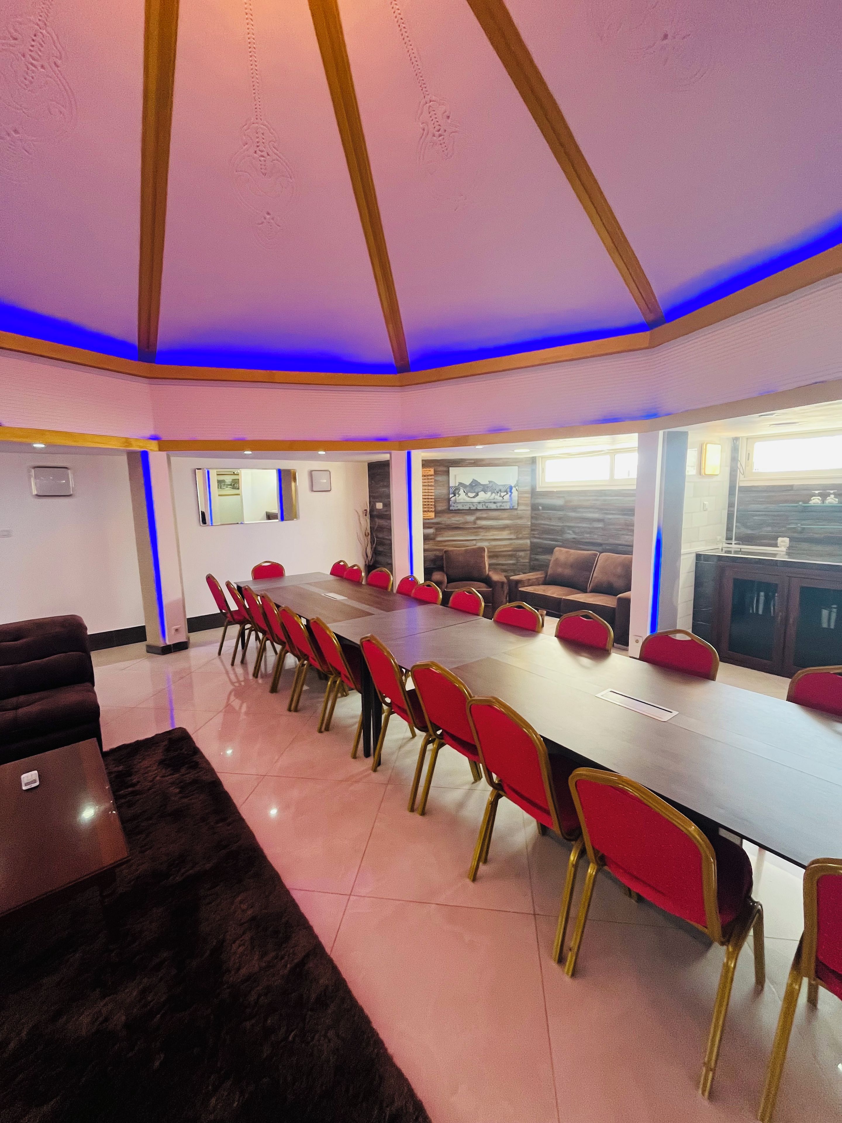 Un salón de conferencias con una mesa larga, sillas rojas y un diseño moderno en el techo.