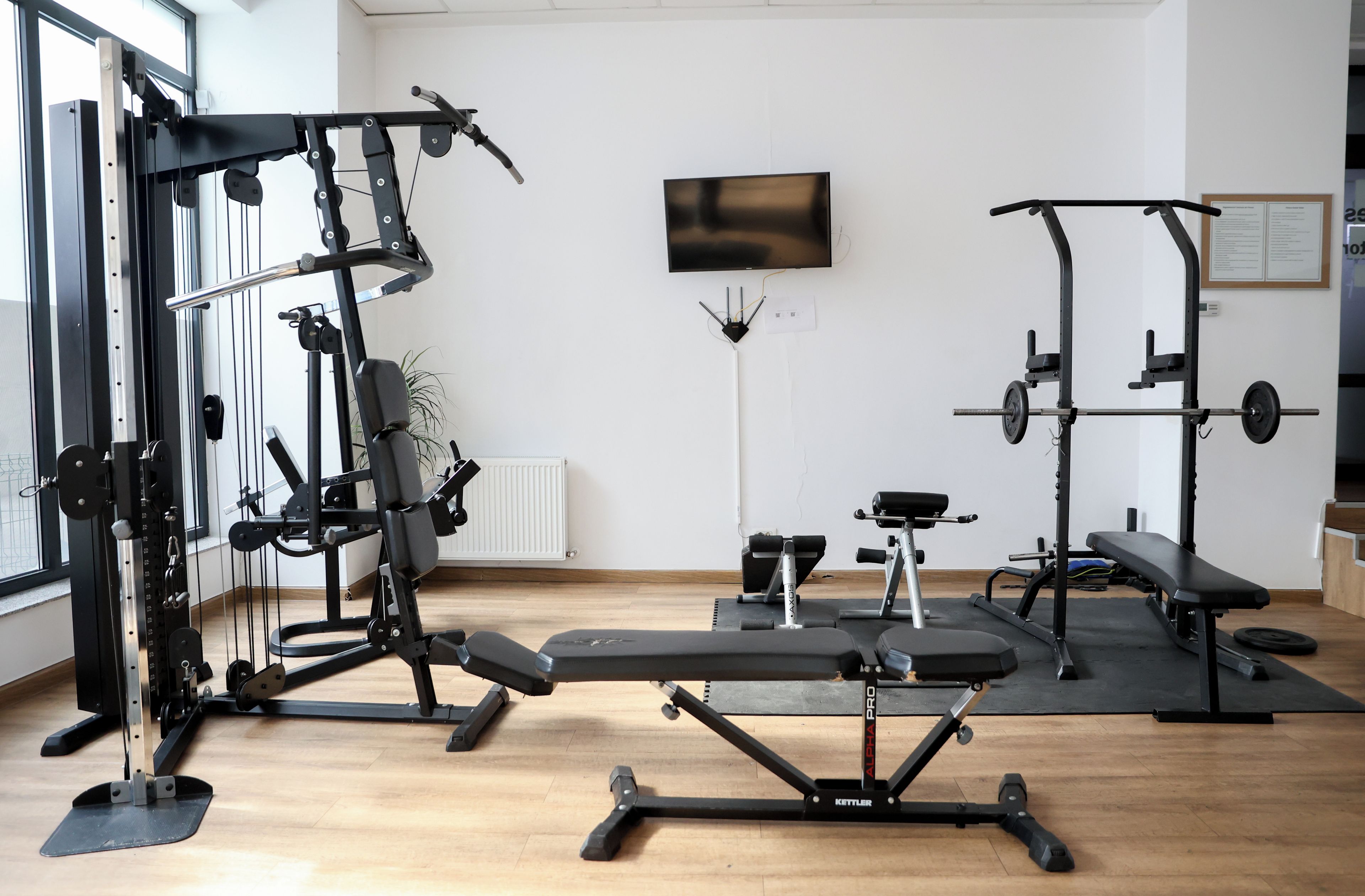 A gym with various exercise equipment, a bench, and a television on the wall.