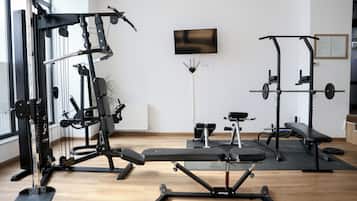 A gym with various exercise equipment, a bench, and a television on the wall.