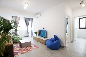 A modern living room with a flat-screen TV, a blue bean bag, a potted plant, and a colorful rug. - Vitan Central Oasis Bucharest (Bucharest)