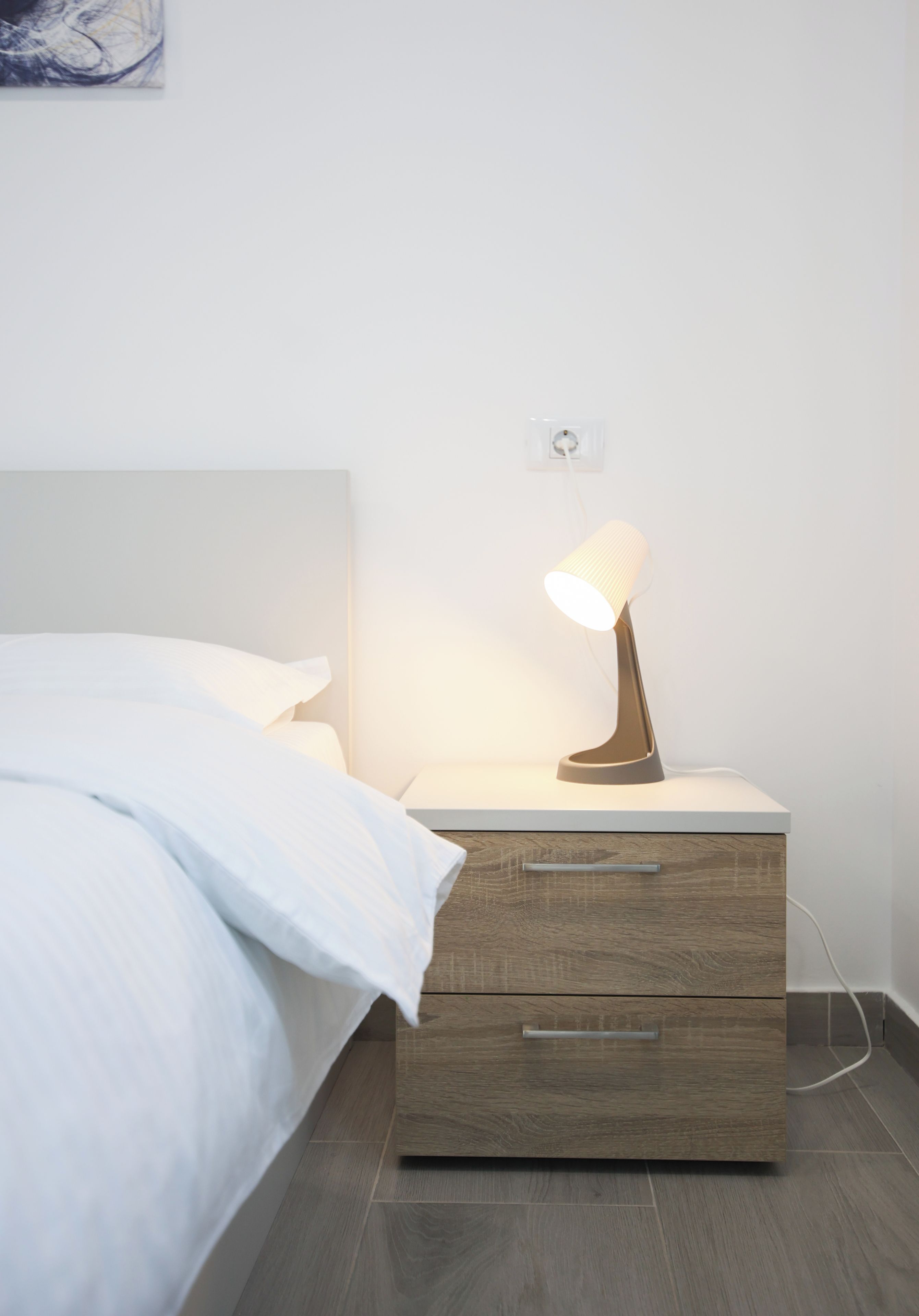 A modern bedroom with a bed, a bedside table with a lamp, and a drawer unit.