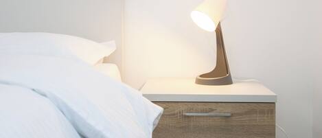A modern bedroom with a bed, a bedside table with a lamp, and a drawer unit.