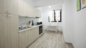 A compact kitchen with light wood cabinets, a stainless steel sink, and a small dining area with a white table and chairs. - Vitan Central Oasis Bucharest (Bucharest)
