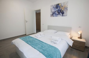 A hotel room with a bed, a nightstand with a lamp, a blue towel, and a painting on the wall. - Vitan Central Oasis Bucharest (Bucharest)