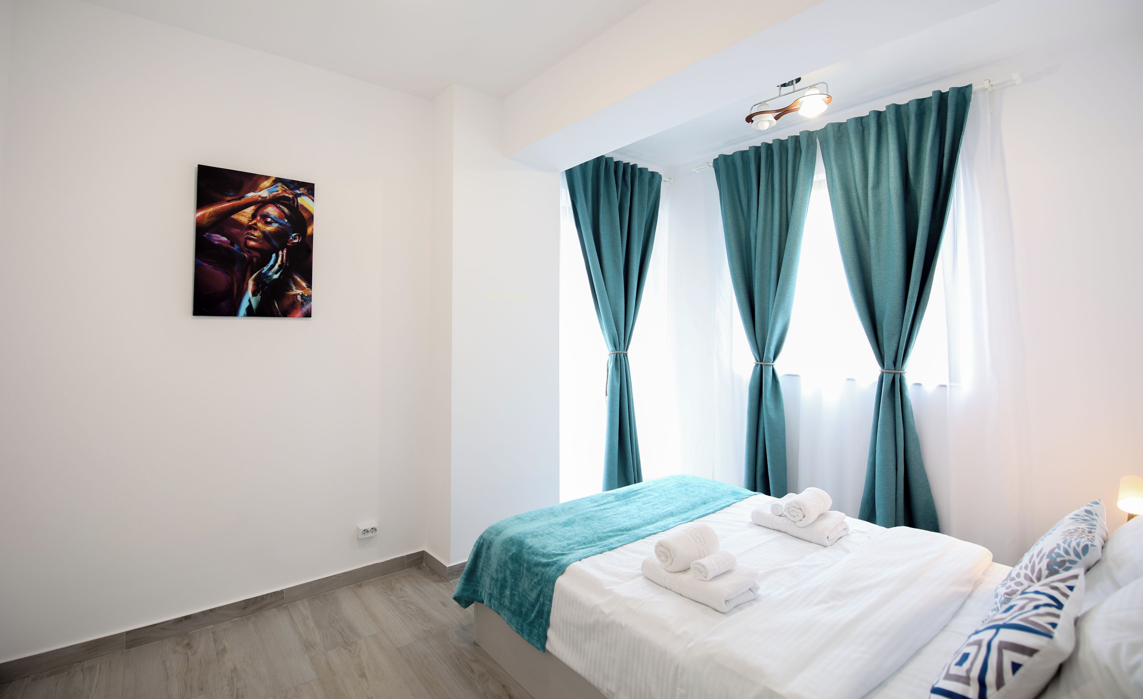 Una habitación de hotel con cama, un cuadro en la pared y cortinas color esmeralda.