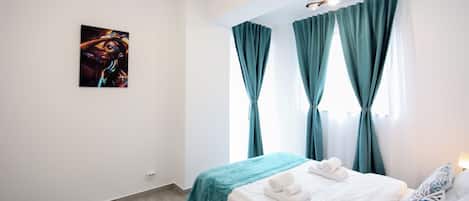 Una habitación de hotel con cama, un cuadro en la pared y cortinas color esmeralda.