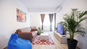 A modern living room with a sofa, a blue bean bag, a coffee table, a TV, a potted plant, and a colorful rug. - Vitan Central Oasis Bucharest (Bucharest)