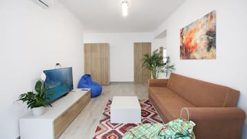 A modern living room with a flat-screen TV, a brown sofa, a blue bean bag, a white coffee table, and a colorful rug.