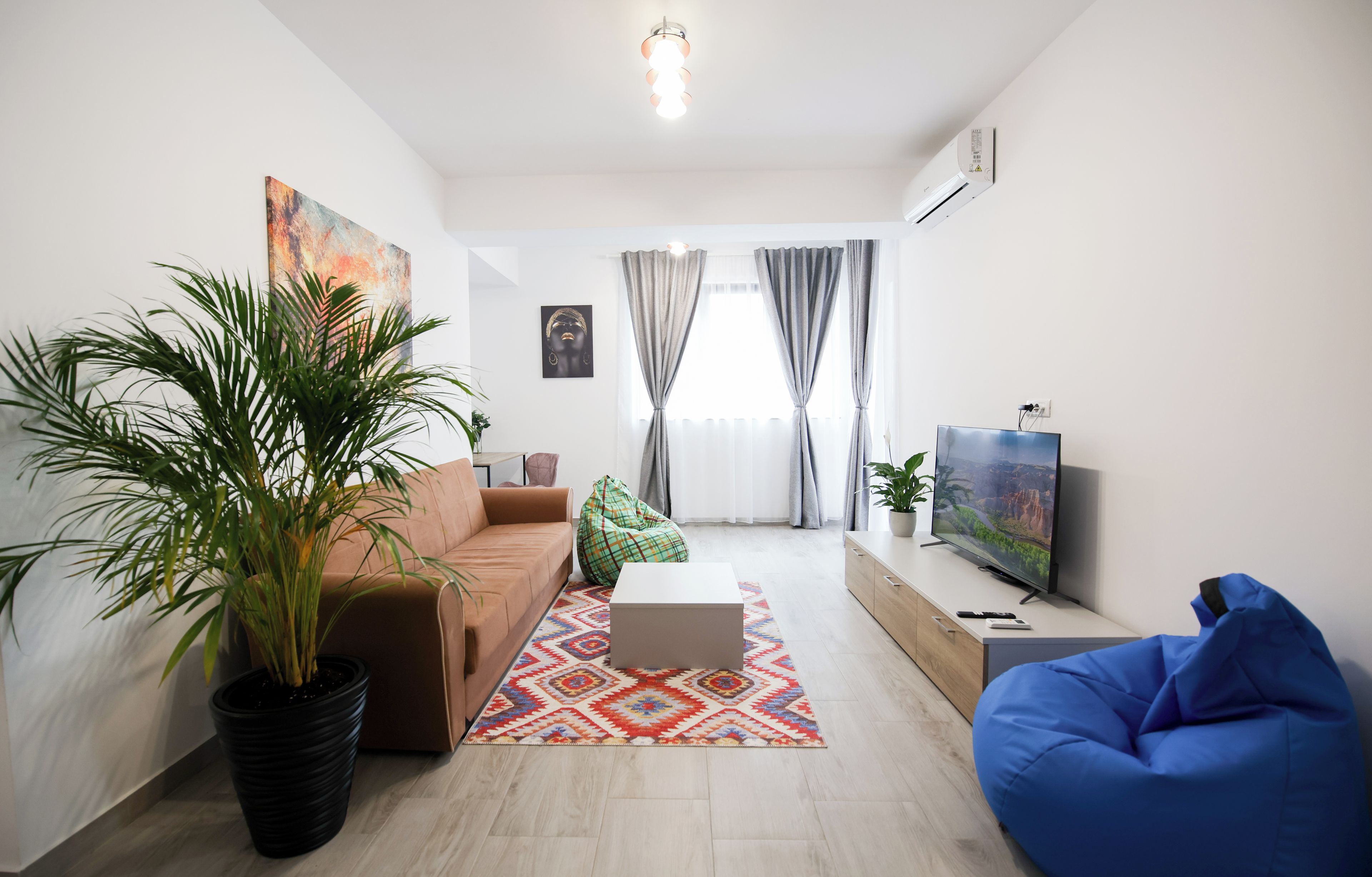 A modern living room with a sofa, a coffee table, a blue bean bag, a television, and a large potted plant.