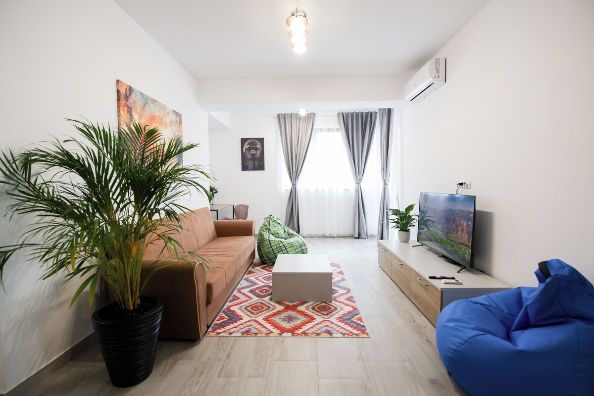 A modern living room with a sofa, a coffee table, a blue bean bag, a television, and a large potted plant.