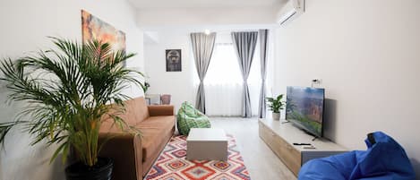 A modern living room with a sofa, a coffee table, a blue bean bag, a television, and a large potted plant.