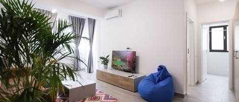 Uma sala de estar moderna com uma janela ampla, um puff azul, uma TV de tela plana e um tapete estampado.