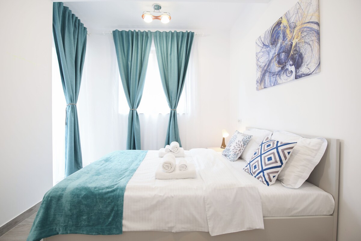 A hotel room with a bed, a bedside lamp, a painting, and curtains.