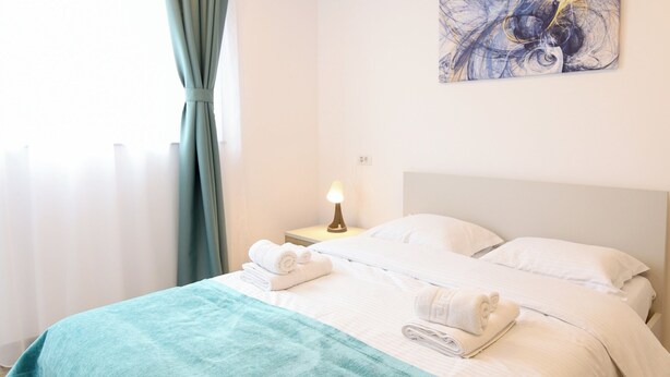 A neatly made bed with a teal blanket, white pillows, and a bedside lamp. - Vitan Central Oasis Bucharest (Bucharest)