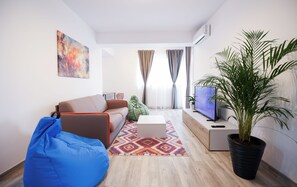 A modern living room with a sofa, a blue bean bag, a coffee table, a TV, a potted plant, and a colorful rug. - Vitan Central Oasis Bucharest (Bucharest)