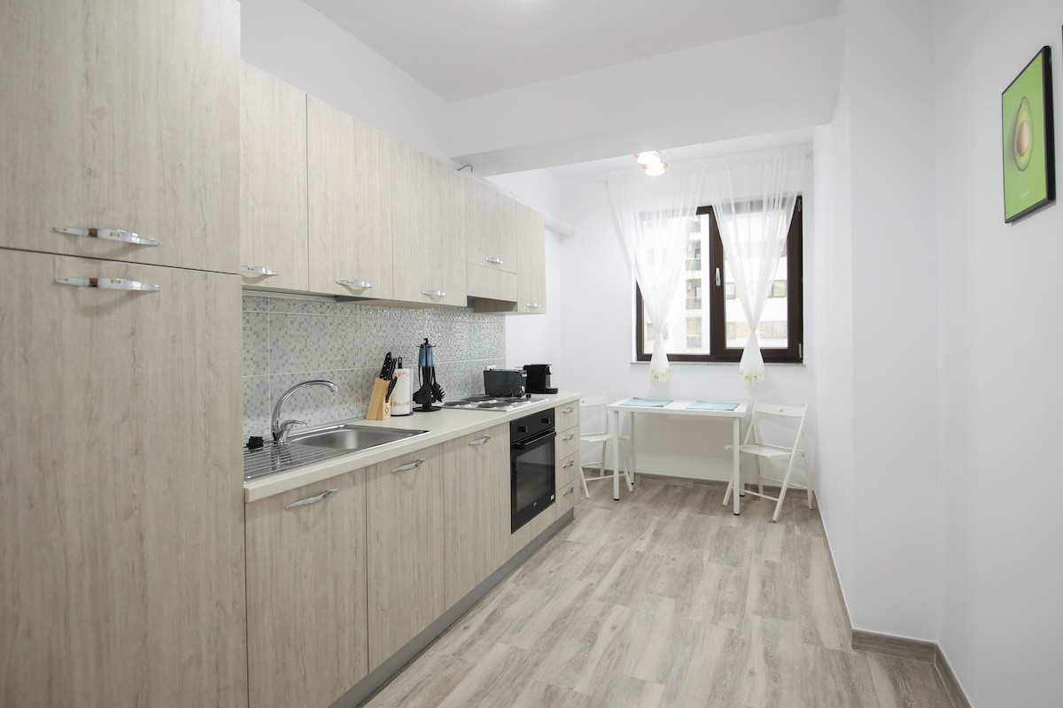 A compact kitchen with light wood cabinets, a stainless steel sink, and a small dining area with a white table and chairs.
