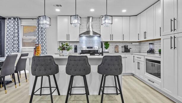 A modern kitchen with white cabinets, a central island with bar stools, pendant lighting, and stainless steel appliances.