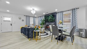 A modern living room with a sofa, dining table, chairs, and a TV.