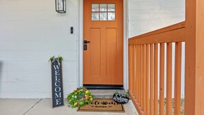 A white brick wall, a wooden door, a welcome sign, a doormat, and a small welcome sign on the ground.