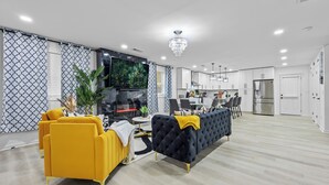 A modern living room with a sofa, a television, and a dining area with chairs and a table.