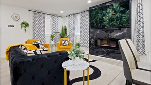 A modern living room with a black sofa, yellow armchairs, a white round table, and a large flat-screen TV.