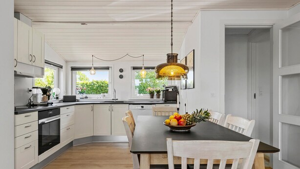 A modern kitchen with white cabinets, a black countertop, and a wooden dining table with chairs. - Lovely home in Broager with WiFi (Broager)