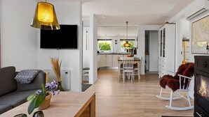 A modern living room with a sofa, a coffee table, and a TV. There is a kitchen area with a dining table and chairs, and a fireplace with a rocking chair. - Lovely home in Broager with WiFi (Broager)
