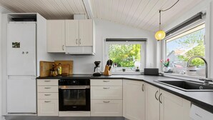 A modern kitchen with white cabinetry, a built-in oven, and a large window providing a view of greenery outside. - Lovely home in Broager with WiFi (Broager)