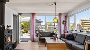 A cozy living room with a fireplace, a sofa, a coffee table, and large windows offering a view of the garden. - Lovely home in Broager with WiFi (Broager)