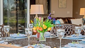 A dining table set with plates, cutlery, and wine glasses, with a vase of flowers in the center. - Intervillas Florida - Villa Royal Sereni Tee (Cape Coral)