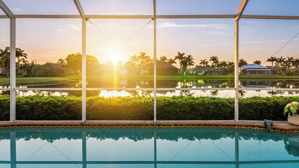 A pool area with a view of a golf course and a body of water during sunset. - Intervillas Florida - Villa Royal Sereni Tee (Cape Coral)