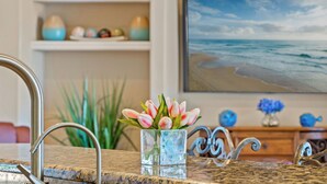 A kitchen counter with a glass vase of pink and white tulips, a stainless steel faucet, and a decorative metal sink. - Intervillas Florida - Villa Royal Sereni Tee (Cape Coral)