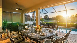 A sunlit outdoor dining area with a pool view, featuring a table set for two with wine glasses and bottles, surrounded by chairs. - Intervillas Florida - Villa Royal Sereni Tee (Cape Coral)