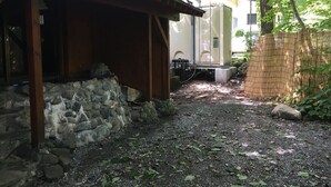 A covered outdoor area with a stone wall, a wooden structure, and a building in the background. - Hakuba Himekawa Onsen Pension Tomato (Hakuba)