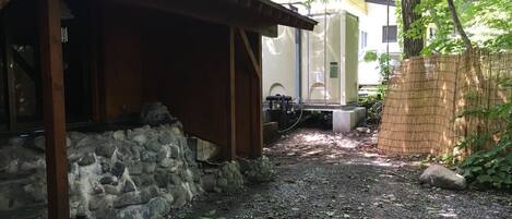 A covered outdoor area with a stone wall, a wooden structure, and a building in the background.