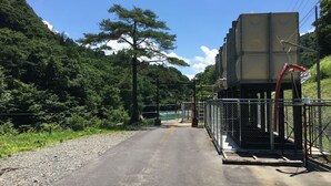 A road leading to a fenced area with a large industrial structure. - Hakuba Himekawa Onsen Pension Tomato (Hakuba)