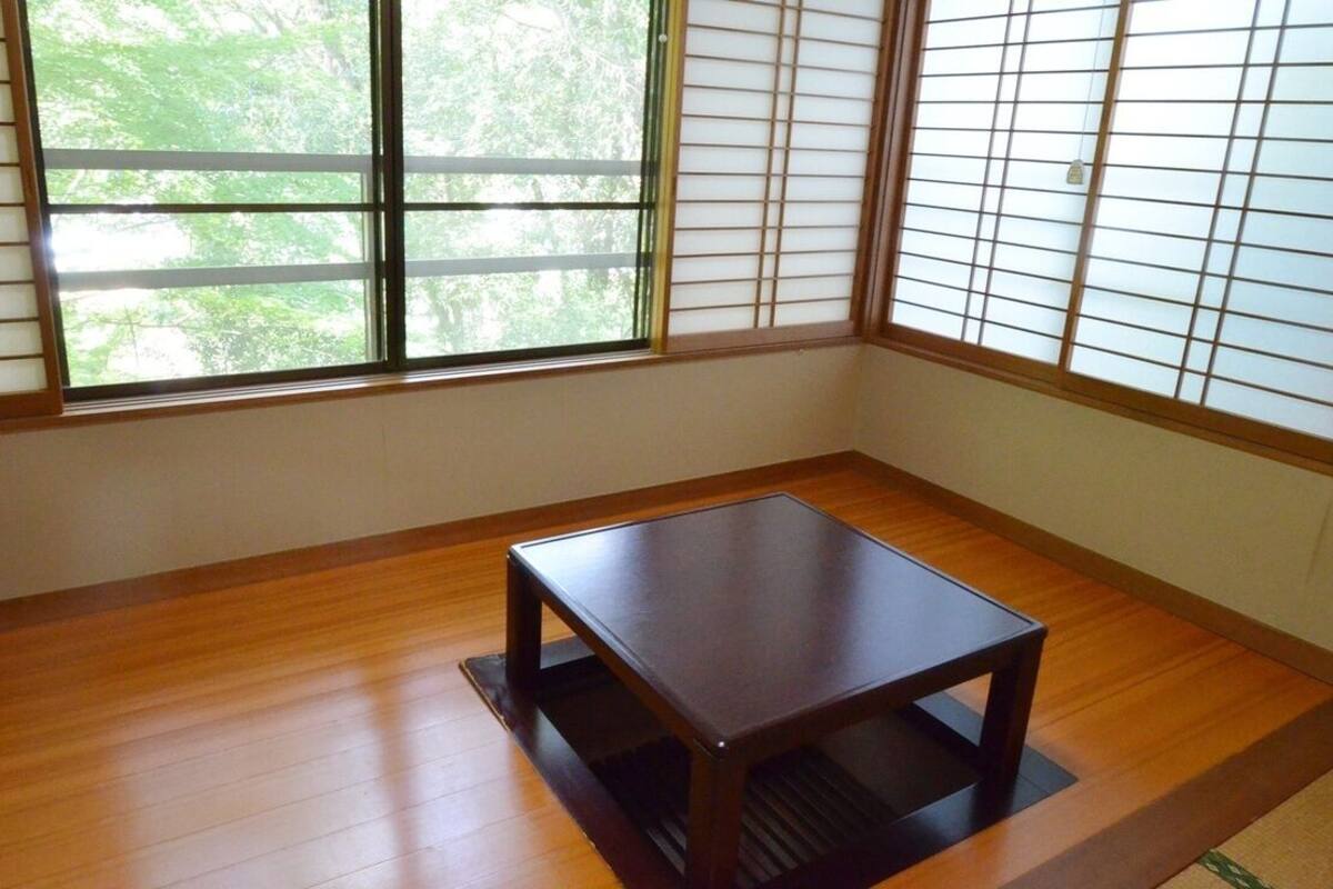 Ein Zimmer mit Holzboden, einem kleinen Tisch und einem Fenster mit Shoji-Bildschirmen.